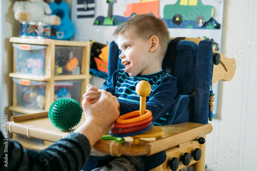 Activities for kids with disabilities. Preschool Activities for Children with Special Needs. Boy with with Cerebral Palsy in special chair play with mom at home.