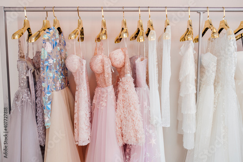 Collection of beautiful evening dresses hanging on rack in dressing room. Clothing on hanger at the modern shop boutique. Clothes hanging on rack, close up