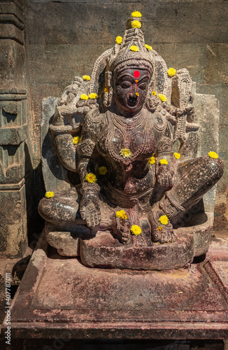 Lakkundi, Karnataka, India - November 6, 2013: Brahma Jinalaya temple. Closeup of damaged black stone statue of padmavati. Yellow flowers dispersed on top.