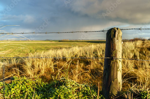 Barbed wire fence with twilight sky and rain clouds over Wadden Island Texel