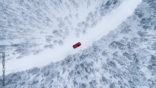 Aerial top view of snow covered forest with winter curving road and red car. Drone photography landscape. 