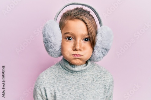 Little beautiful girl wearing fluffy earmuff puffing cheeks with funny face. mouth inflated with air, catching air.