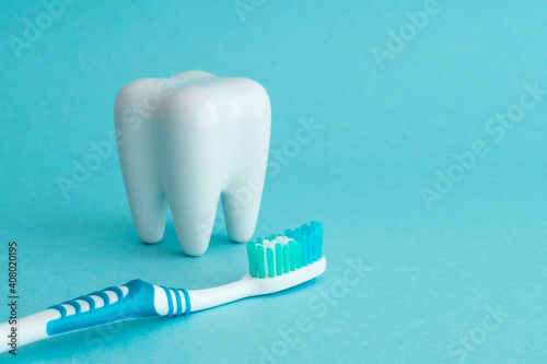 White healthy tooth model and blue dental toothbrush on blue background with copy space. Dental care and healthcare concept.