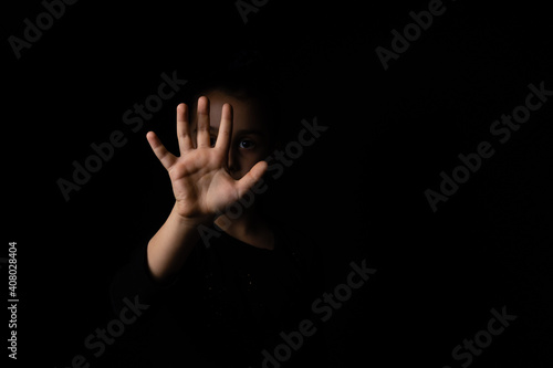 little girl with a raised hand making a stop sign gesture on a black background. Violence, harassment and child abuse prevention concept.