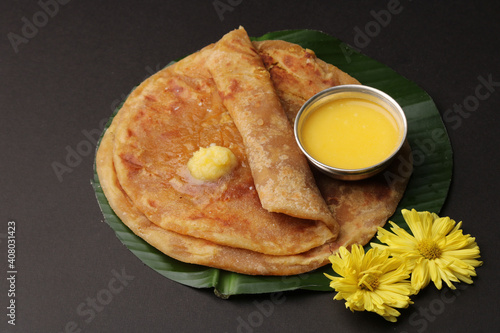 Puran Poli, also known as Holige, is an Indian sweet flatbread from India consumed mostly during Holi festival. Served on banana leaf with pure Ghee over black background.