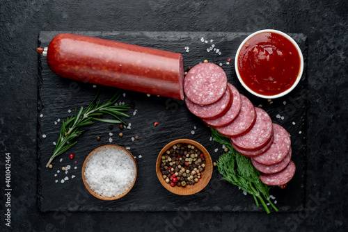 Dry salami sausage with fresh rosemary and spices on a stone background 