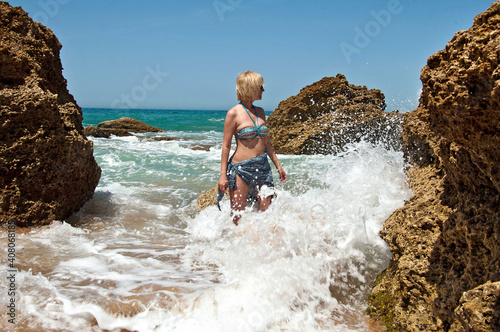 A woman in a bathing suit stands in a lagoon with big waves