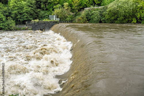 Turbulent water at a weir of a river in flood after extreme weather. No people.