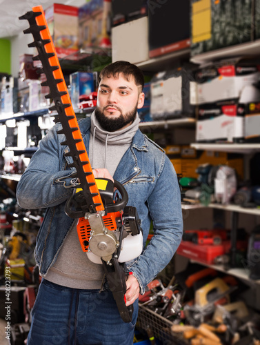 adult serious man with an electric brush cutter in hardware store