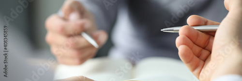 Close up of male hands holding sheet of paper with pen while sitting at the desk in the office. Work and business concept