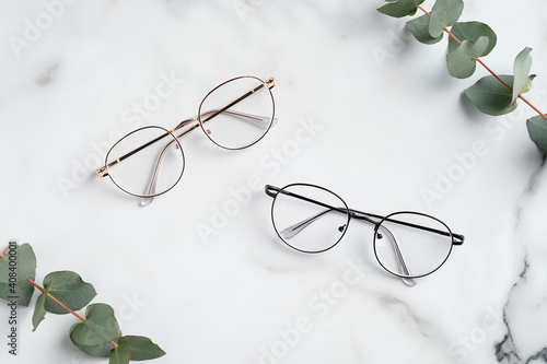 Women's glasses and eucalyptus leaves on marble table top view