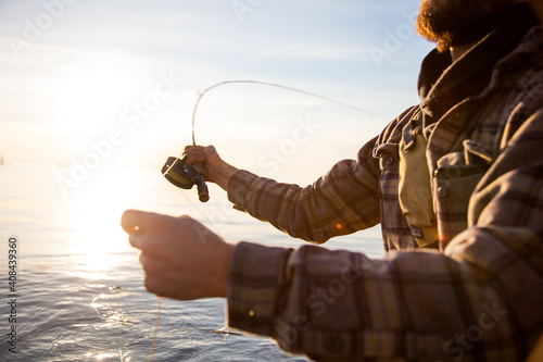 A close up of a fly fisherman wearing a plaid shirt, holding a rod and reel while wading in the water in Vancouver, British Columbia