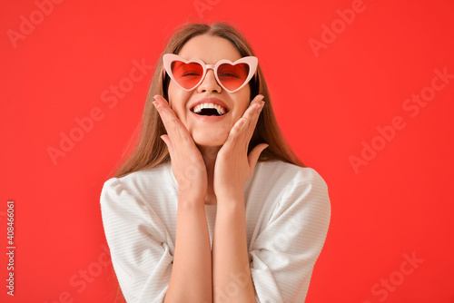 Beautiful young woman in stylish heart-shaped sunglasses on color background