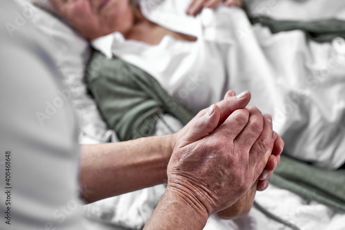 elderly man crying and mourning the loss of his wife, sitting by her side. focus on hands. coronavirus, covid-19 concept