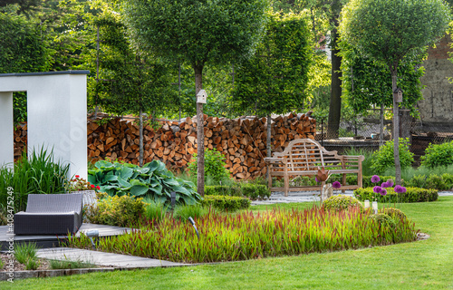  A relaxing spot for a warm, summer day - a stylish, wooden terrace with wicker garden furniture, cushions, plants and flowers 