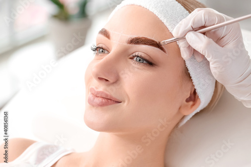 Young woman undergoing eyebrow correction procedure in beauty salon