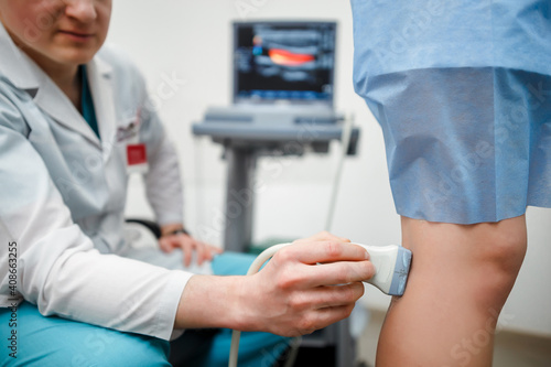 Orthopedist doctor doing ultrasound examination of patient's leg veins in his office. Young woman passing ultrasound scan in clinic. Doctor work. Medical research.