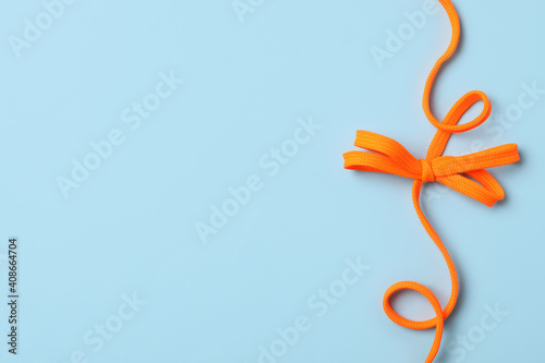 Orange shoelace on light blue background, top view. Space for text