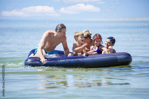 Siblings, their friends and father having fun on inflatable air mattress. Young children and dad enjoying summer vacation on seaside.