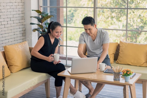 Asian man and woman family in casual outfit sitting in living room drinking coffee and using laptop together in happy and smile emotion