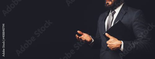 man in suit holding a bible in his arm speaking to another person on a black background