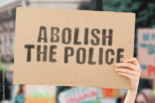 The phrase " Abolish the police " on a banner in men's hand with blurred background. Dangerous. Aggressive. Danger. Conflict. Behaviour. Battle. Fight. Illegal. Angry