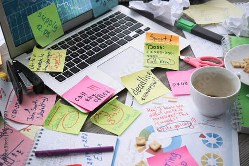 Laptop, notes and office stationery in mess on desk. Overwhelmed with work