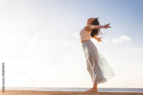 Freedom and empowerment female concept with young girl standing and enjoying outdoor nature - young girl love free independent life and vacation - sky and ocean in background