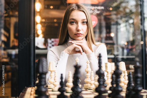 Beautiful girl play chess, queen’s gambit play and everyone wins, a smart and pensive face. White and black chess pieces are displayed on the board. mental game, a lot of time to last, not for fools