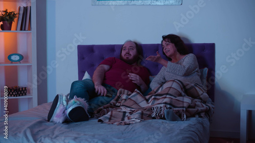 Happy smiling senior mother talking to adult son relaxing on bed at home