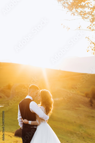 Tender newlyweds hugging on top of a mountain at sunset.