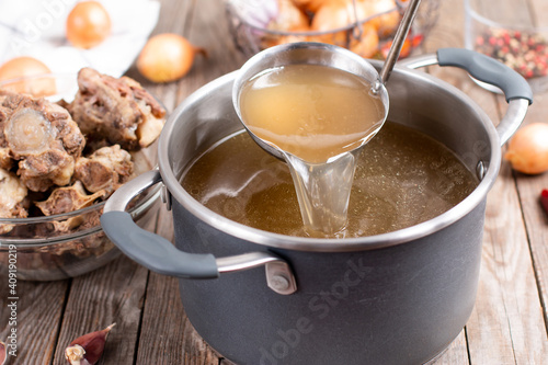 Saucepan with bouillon with a ladle on a wooden table. Bone broth