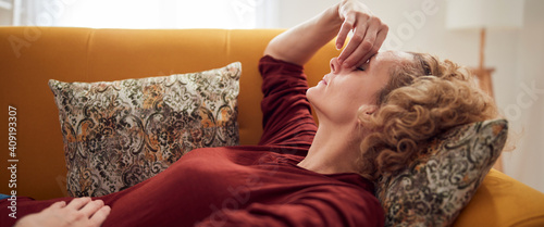 Woman with sinus pain, headache and stomach problems, lying on a couch at home.