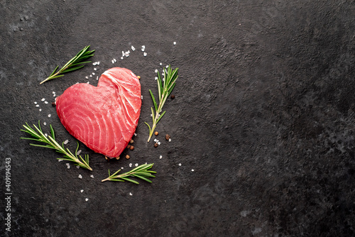 Heart shaped raw tuna steak with rosemary and spices on stone background with copy space for your text