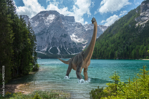 Brachiosaurus walks alone into cold lake before dinosaurs extinction. Snow on the mountains in the background.