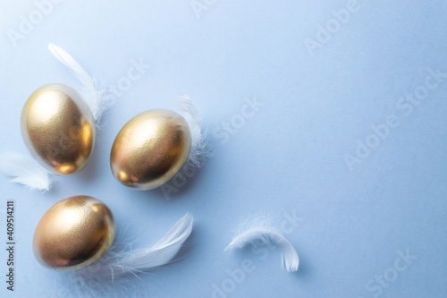 Easter eggs Golden color egg with white feathers on pastel blue background in Happy Easter decoration. Festive decoration in flat lay.