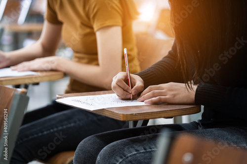 Young female university students concentrate on doing examinations in the classroom. Girl students seriously write the exercise of the examinations in the classroom.