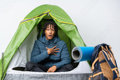 Young african american man inside a camping green tent surprised and shocked while looking right