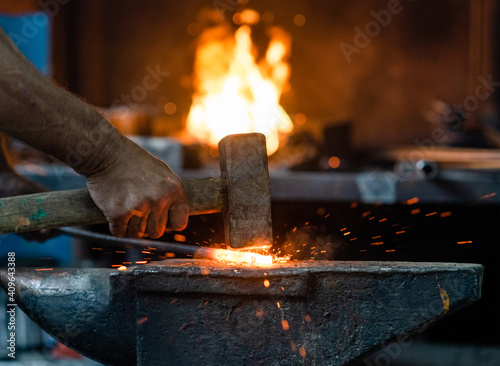 Close up blacksmith working metal with hammer on the anvil in the forge