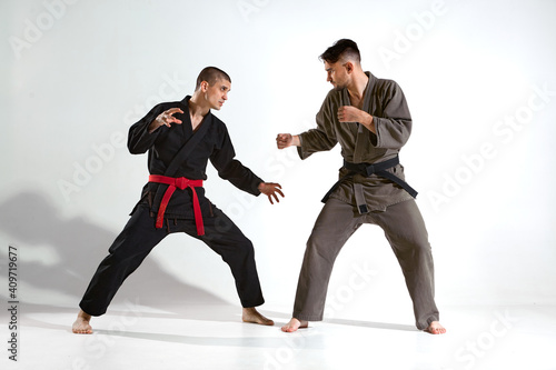 Athletic males in kimono fighting during kudo workout on white studio background with copy space, martial arts concept