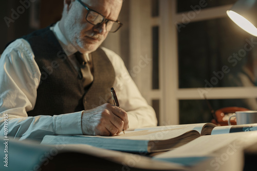 Academic professor writing down notes and reading a book