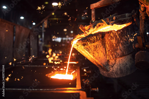 Molten metal casting in foundry. Filling mold with hot liquid iron and producing iron components in steel plant.