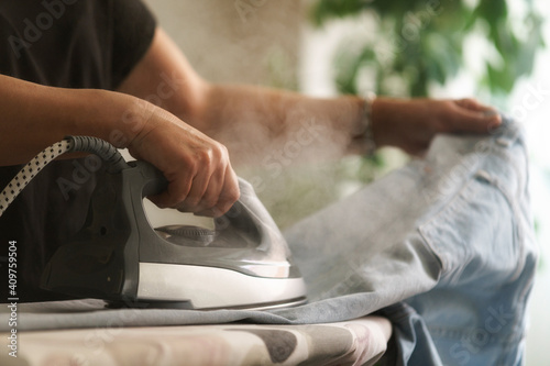 Primer plano de mujer ama de casa planchando los vaqueros con vapor en el salón de su hogar.