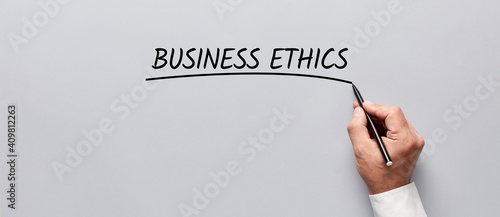 Businessman hand underlining the word business ethics on gray background. The ethics of business.
