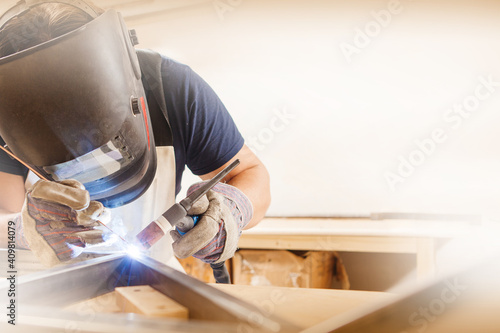 Male in face mask welds with argon-arc welding