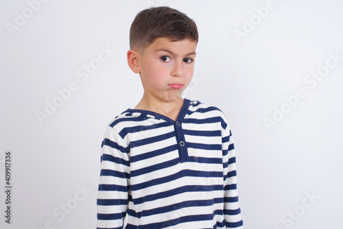 little cute boy kid wearing red stripped t-shirt against white wall with snobbish expression curving lips and raising eyebrows, looking with doubtful and skeptical expression, suspect and doubt.