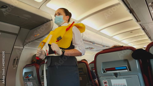 Woman stewardess flight attendant in face mask presenting life vest on board before the flight departure