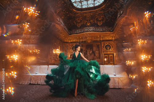Portrait of a beautiful young girl in a Haute couture green dress standing in a luxurious gold interior.