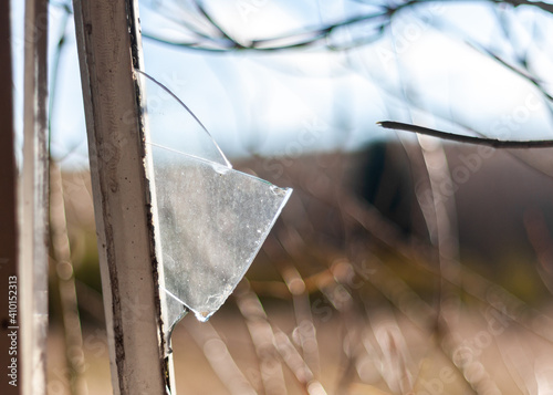 Broken glass following burglary in open window with metal frame sharp edge shard of glass sticking out in derelict building after vandalism