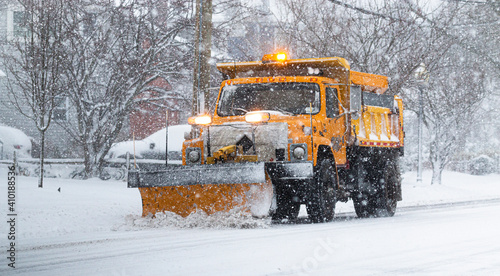 Yellow snowplow clearing a road during a snow storm